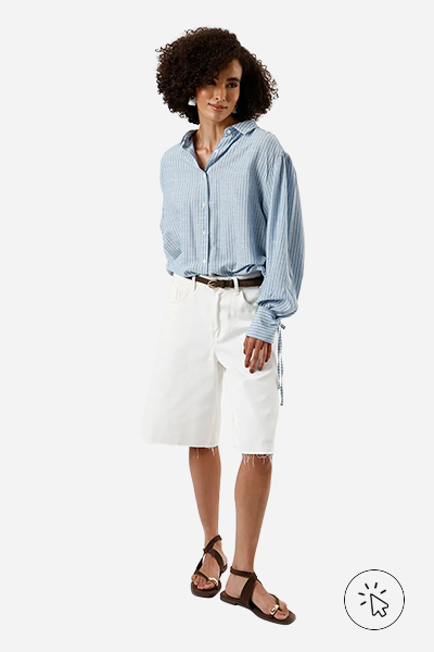 Modelo veste camisa com manga bufante listrada azul, bermuda jeans de sarja off-white, cinto marrom e rasteirinha marrom. - como usar camisa listrada