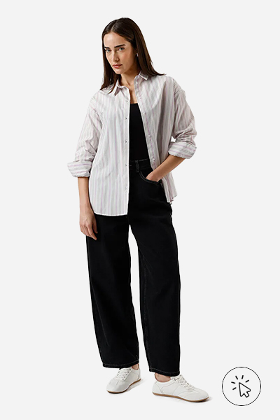 Modelo veste camisa oversized listrada de manga longa lilás, regata preta, baggy jeans escuro e tênis branco.- como usar camisa listrada