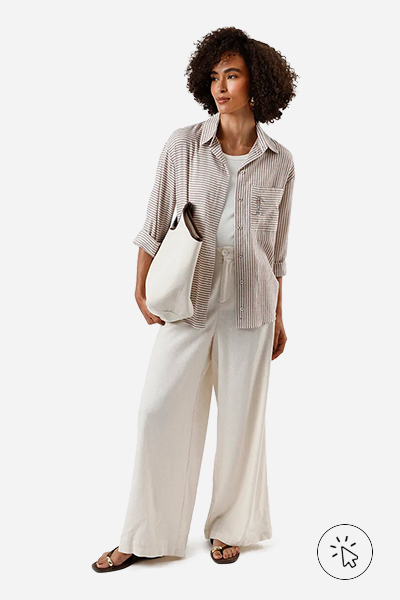 Modelo veste camisa oversized listrada de manga longa marrom, regata off-white, wide leg com linho bege, bolsa shopper bege e rasteirinha marrom.- como usar camisa listrada