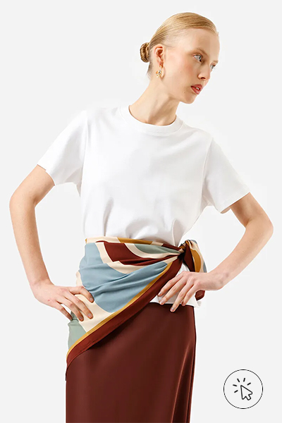 Modelo veste camiseta branca, saia mídi marrom e lenço com estampa abstrata azul e marrom amarrado na cintura