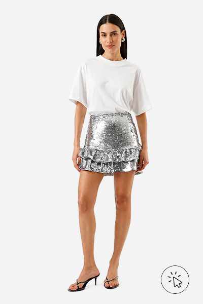 Modelo veste saia curta feminina de paetê cinza prata com camiseta branca