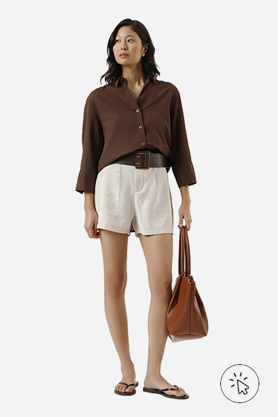 A modelo está usando uma camisa marrom, short off-white e cinto preto.