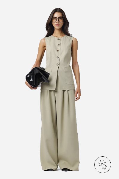 A modelo está usando um colete de alfaiataria e uma calça bem ampla. Ela está segurando uma bolsa preta.  - tecido linho - o que é linho - como lavar roupa de linho - como passar roupa de linho - como é feito o linho 