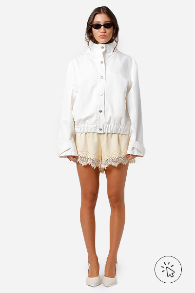 Modelo veste jaqueta off-white, saia acetinada com renda bege e Scarpin anabela slingback off-white