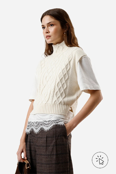 modelo veste colete de tricô off-white sobrepondo uma camiseta branca com barrado de renda e uma calça de alfaiataria xadrez - look com colete de tricô