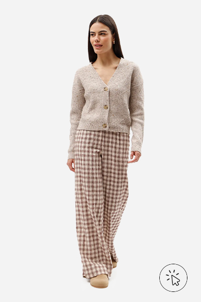 A modelo está usando uma calça xadrez, estilo de pijama, e um cardigan bege. Nos pés, ela usa uma clog - estilo grunge - o que é o estilo grunge
