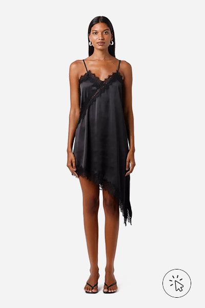 A modelo está usando um vestido acetinado preto com barra assimétrica, com renda e tamanco nos pés - estilo grunge - o que é o estilo grunge