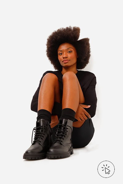 A modelo está sentanda no chão, com short e blusa de manga longa preta e uma bota coturno - estilo grunge - o que é o estilo grunge